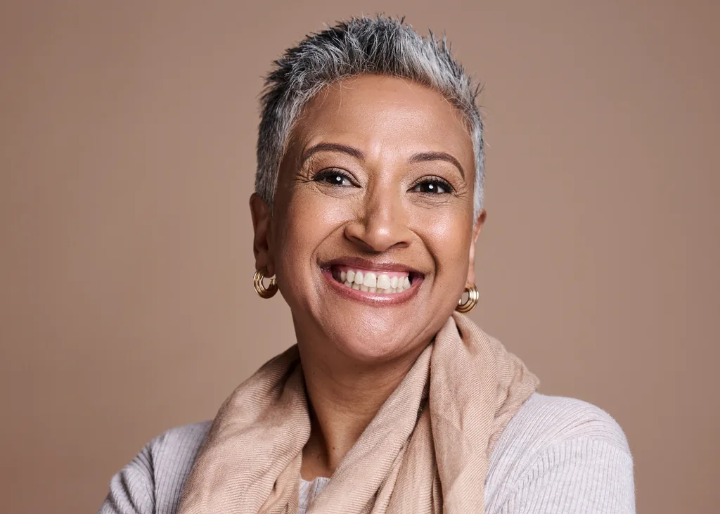 Foto profissional de mulher grisalha sorrindo, fundo bege